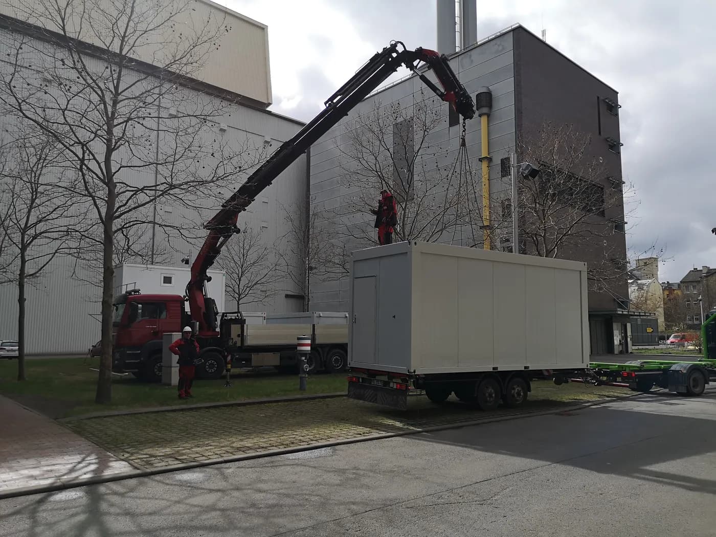 Zwei Monteure montieren mit einem Kran einen Container in einem städtischen Industrieumfeld – Teil eines professionellen Einsatzes der Mobil-Raum GmbH vor Ort.